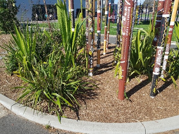 Garden bed with green plants, with long, flat leaves, and decorated totem poles.