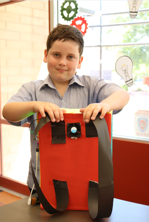 Image of a primary school boy holding up an invention