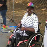 Girl sitting in wheelchair bouncing a ball on a tennis racquet.