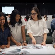 Screenshot of female university students standing around a table