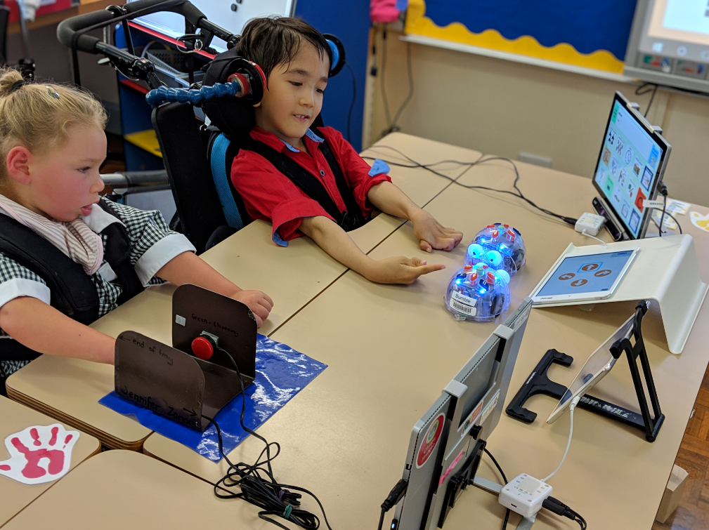 Photo of two primary school children playing with robotics that are connected to tablets.