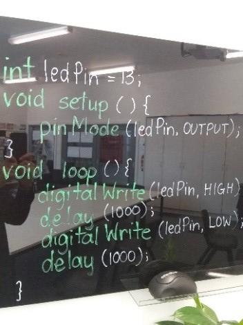 LED code on a whiteboard. It says 'Line 1: int Led Pin equals 13 semi colon. Line 2: void setup open bracket close bracket open curly bracket. Line 3: pin Mode open bracket led Pin comma output close bracket semi colon. Line 4: close curly bracket. Line 5: void loop open bracket close bracket open curly bracket. Line 6: digital write open bracket led pin comma high close bracket. Line 7: delay open bracket 1000 close bracket semi colon. Line 8: digital write open bracket led pin comma low close bracket. Line 9: delay open bracket 1000 close bracket semi colon. Line 10: close curly bracket.'