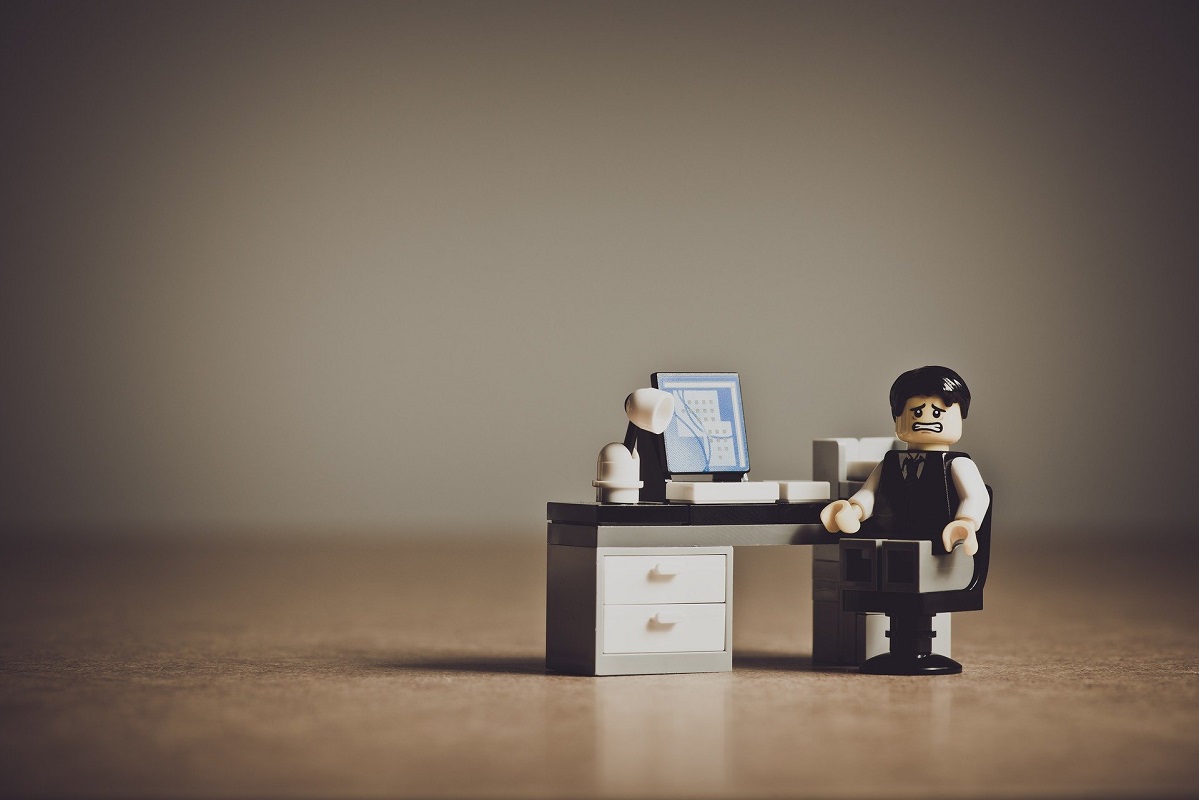 Photo of a Lego figure sitting at desk with frustrated face.
